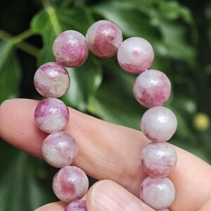 May include: A beaded bracelet featuring smooth, round gemstone beads in varying shades of pink, magenta, and white. Each bead displays a unique, marbled pattern with translucent and opaque sections, strung together to form a continuous circular loop.