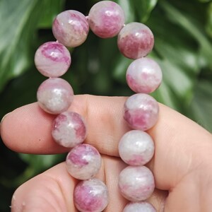 May include: A strand of round, polished beads featuring a marbled pattern of vibrant magenta, soft pink, and opaque white. The beads are strung together in a vertical arrangement, showcasing a smooth, glossy texture and varied color distribution.