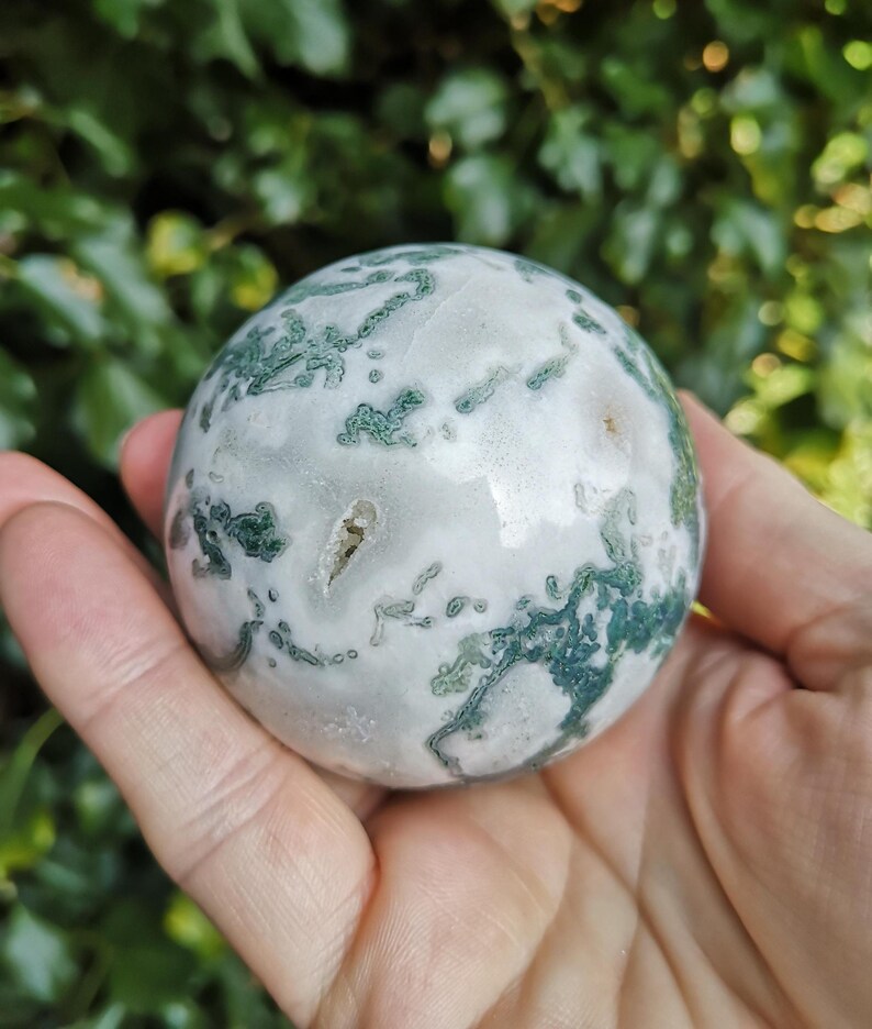 May include: A green and white agate sphere, polished to a smooth finish. The sphere has a swirling pattern of green and white, with a few small white spots.