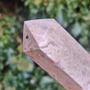 May include: A pink and white polished crystal point with a faceted shape. The crystal has a natural, organic pattern of white and pink.