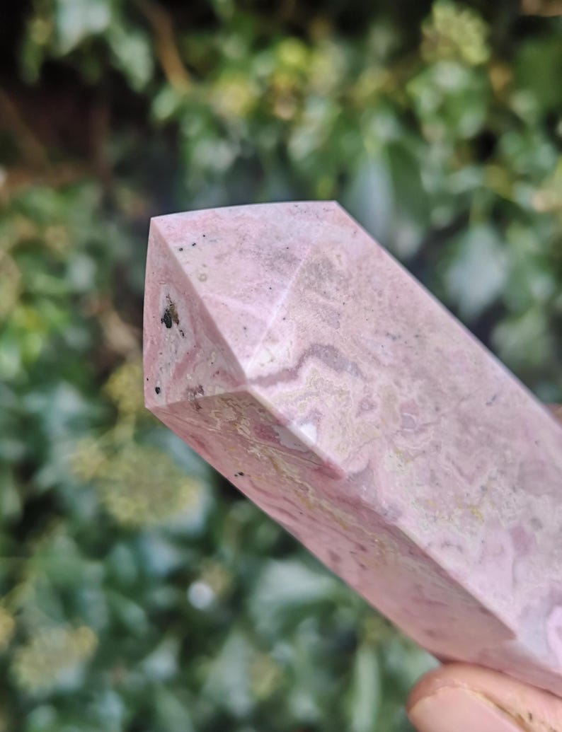 May include: A pink and white polished crystal point with a faceted shape. The crystal has a natural, organic pattern of white and pink.