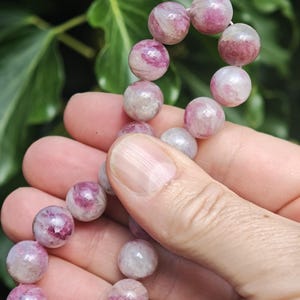 May include: A strand of round, polished beads featuring a mix of translucent white and vibrant pink or magenta hues. The beads are strung together in a continuous line, showcasing natural variations in color and internal texture within each stone.