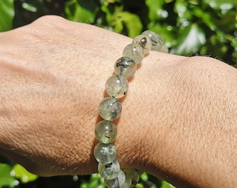 May include: A green and black gemstone bracelet with round beads. The bracelet is made of natural stones and is worn on a person's wrist.