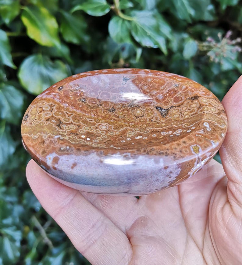 May include: A brown and white agate bowl with a swirling pattern. The bowl is smooth and polished, and it has a natural, organic shape.