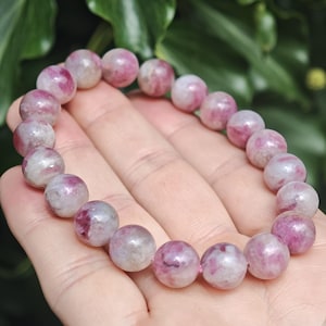 May include: A stretch bracelet composed of round, polished beads featuring a marbled pattern of deep magenta, soft pink, and translucent white tones. The beads are strung together in a continuous circular loop, showcasing natural color variations.