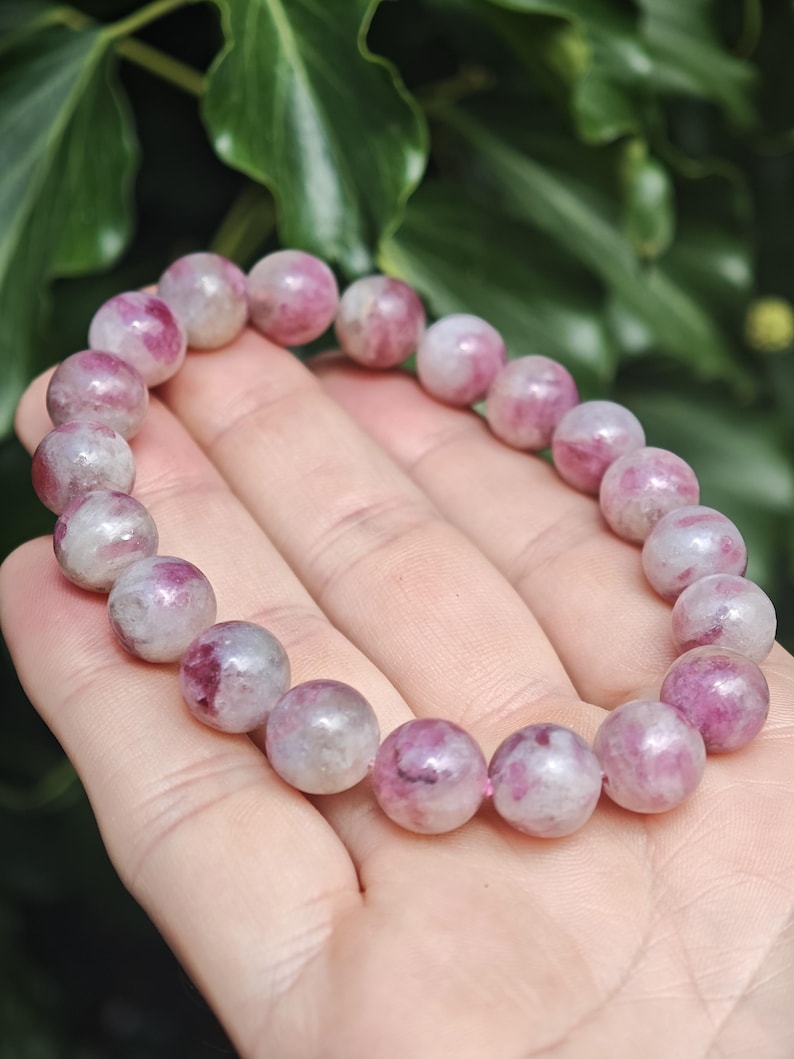 May include: A stretch bracelet composed of round, polished beads featuring a marbled pattern of deep magenta, soft pink, and translucent white tones. The beads are strung together in a continuous circular loop, showcasing natural color variations.