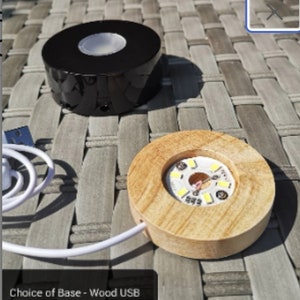 May include: Two round display bases for showcasing small objects. One base is black and battery-powered, the other is wood and USB-powered. Both bases have a clear circular platform with LED lights.