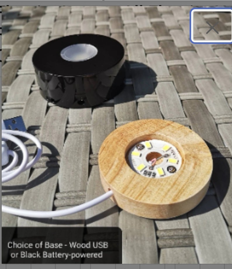 May include: Two round display bases for showcasing small objects. One base is black and battery-powered, the other is wood and USB-powered. Both bases have a clear circular platform with LED lights.