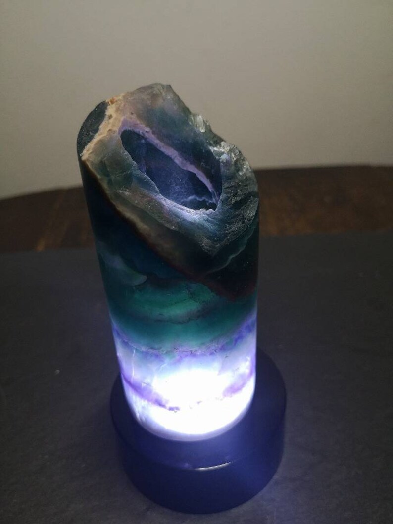 May include: A green, purple, and blue fluorite crystal lamp with a white light shining through the crystal. The lamp is on a black base.