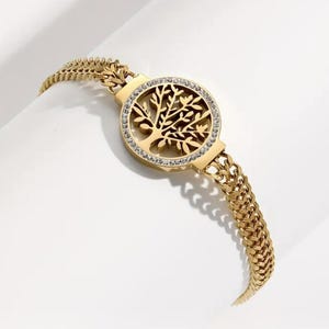 May include: A gold-tone bracelet with a circular charm featuring a tree of life design with clear rhinestones. The bracelet has a double chain link design.