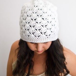 Puede incluir: Un gorro blanco de ganchillo con un patrón de encaje. El gorro lo lleva una persona con el pelo largo y oscuro.