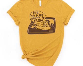 May include: Mustard yellow t-shirt with a brown graphic of a man driving a car and a speech bubble that says "It'd be a lot cooler if ya did."