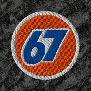 May include: Embroidered patch with the number 67 in blue, within an orange circle and a white border. The patch has a textured look, set against a dark grey background.