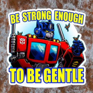 Peut inclure: Un autocollant représentant Optimus Prime de Transformers, en rouge, bleu et jaune. Le texte "BE STRONG ENOUGH TO BE GENTLE" est affiché en jaune. Deux petits oiseaux sont perchés près du robot.