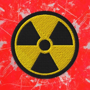 Peut inclure: Écusson brodé avec le symbole de radiation, un trèfle jaune dans un cercle noir, sur fond rouge avec des marques blanches. Idéal pour vêtements ou accessoires.