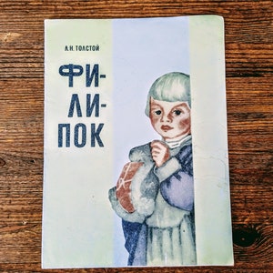 May include: A vintage book cover with a light blue background. The title "ФРИ-ЛИ-ПОК" is printed in black. A young child with blonde hair is pictured holding a stuffed animal. The child is wearing a blue and white dress.