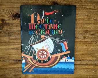 May include: A hardcover book with a black cover featuring a colorful illustration of a ship with a large helm and sails. The book's title, in orange, red, and blue, is written in a foreign language. The background is a starry night sky.