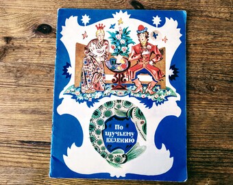 May include: A vintage children's book cover with a blue background and a white border. The cover features a colorful illustration of a king and queen sitting on a throne, with a fish and the text "По щучьему велению" in the center.