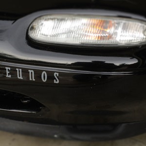 May include: Black car with a front bumper that has the word "Eunos" written on it.