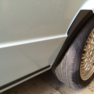 以下が含まれることがあります： 薄い青色の車に黒いタイヤと銀色のホイールが付いている。 車のボディの下部には黒いトリムがある。