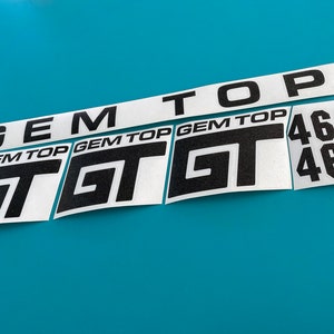 以下が含まれることがあります： 黒い文字が書かれた白いステッカーが5枚。ステッカーには「GEM TOP」と「GT 460」と書かれています。