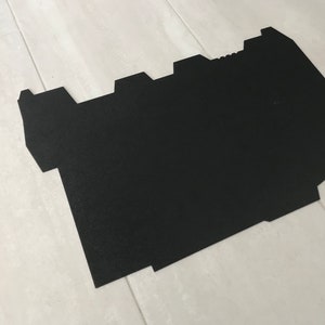 以下が含まれることがあります： 黒く、不規則な形をした平らな素材。床のマットか段ボールの可能性があります。