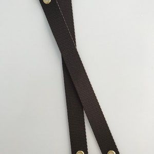 May include: Two brown straps with gold metal eyelets. The straps are crossed over each other.