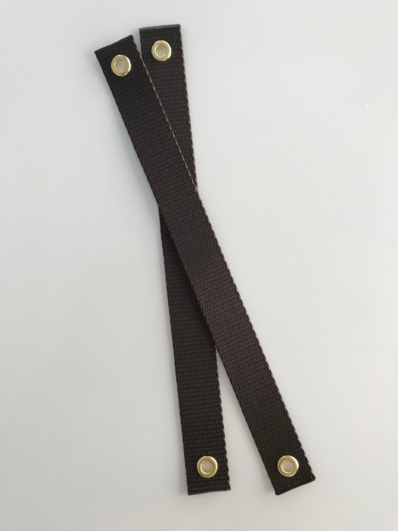 May include: Two brown straps with gold metal eyelets. The straps are crossed over each other.