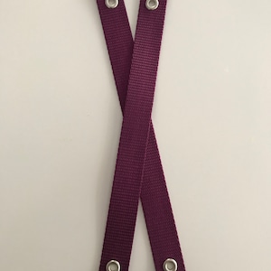 May include: Two burgundy straps with silver metal eyelets. The straps are crossed over each other.