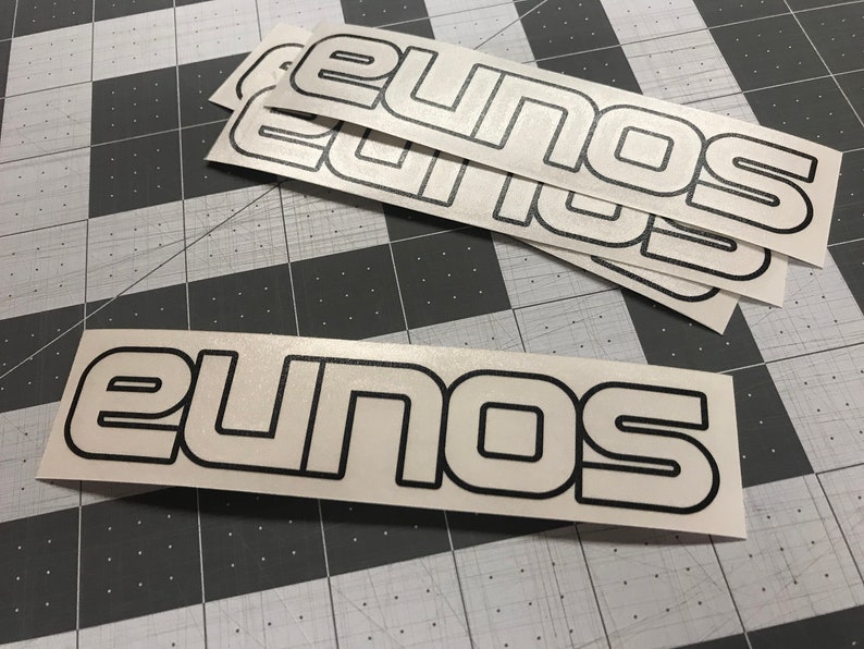 May include: A set of four white vinyl stickers with black outlines that read "Eunos".