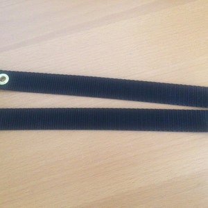 May include: Two black straps with metal eyelets. The straps are approximately 2.5 cm wide and have a woven texture.