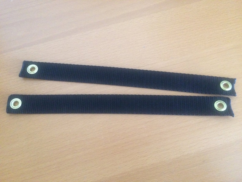 May include: Two black straps with metal eyelets. The straps are approximately 2.5 cm wide and have a woven texture.