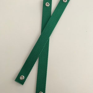 May include: Two green straps with silver metal eyelets. The straps are approximately 45 cm long.