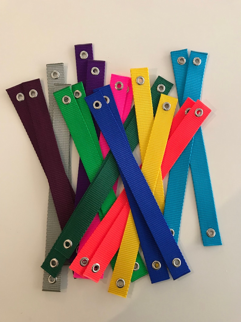 May include: Assortment of colourful fabric straps with metal eyelets. The straps are in various colours, including purple, grey, green, pink, orange, yellow, blue, and turquoise.