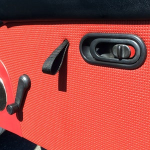 May include: Red car door panel with a black door handle, a black window crank, and a black strap.
