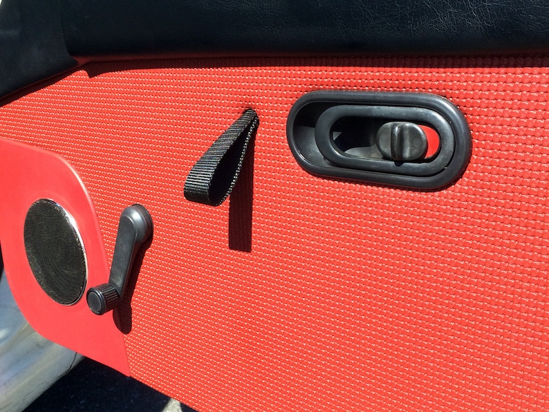 May include: Red car door panel with a black door handle, a black window crank, and a black strap.