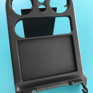 Pode incluir: Painel de painel de carro de plástico preto com três aberturas redondas e uma abertura retangular. O painel tem uma superfície texturizada.