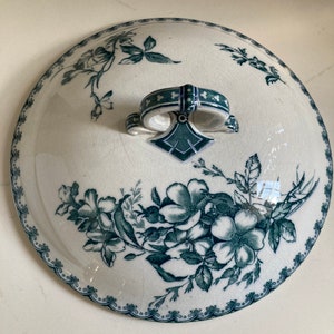 May include: White ceramic lid with a green floral design and a green handle. The lid has a scalloped edge and a decorative border.