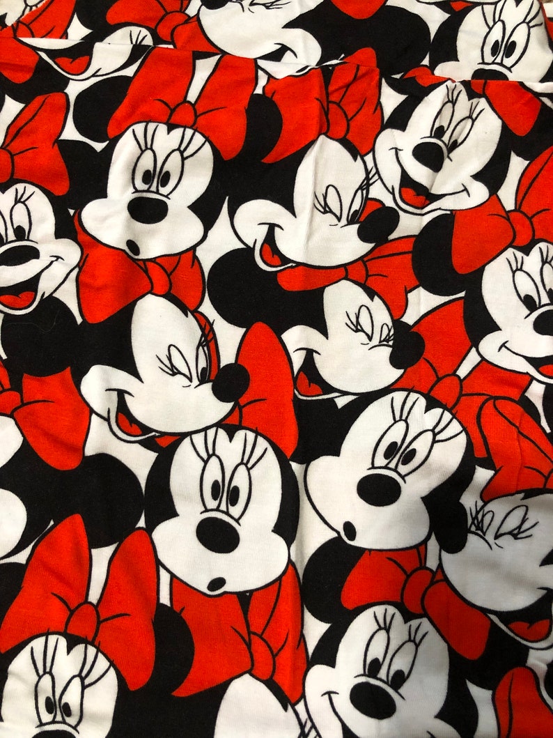 Puede incluir: Una tela blanca con un patr&oacute;n repetido de lazos rojos y caras de dibujos animados en blanco y negro de Minnie Mouse.
