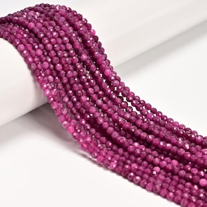 May include: Strands of faceted, round, deep magenta beads. The beads have a sparkling, polished appearance and are strung together, creating a flowing, textured effect. The beads are likely used for jewelry making or crafting.