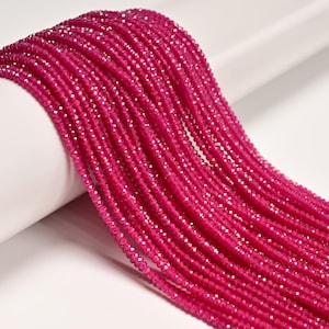 May include: Close-up of strands of faceted, hot pink gemstone beads. The beads are strung together, creating a flowing, textured appearance. The beads are displayed against a white background.