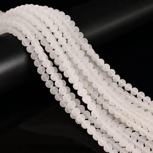 May include: Strands of white, matte-finish round beads. The beads are uniform in size and shape, creating a smooth, flowing texture. The beads are strung together, ready for jewelry making or other craft projects.