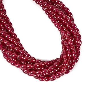 May include: A multi-strand necklace composed of numerous small, polished, deep red oval-shaped beads. The beads are arranged in several parallel rows, creating a dense, layered appearance with a consistent glossy finish throughout the piece.