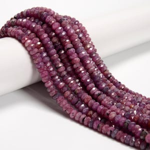 May include: Strands of faceted, deep red-purple gemstone beads. The beads have a slightly irregular shape and are strung together, creating a flowing, textured appearance. The beads are displayed against a white background.