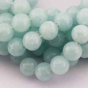May include: Close-up of a strand of round, light blue beads. The beads are smooth and appear to be made of a polished stone or glass. The beads are strung together, creating a necklace or bracelet.