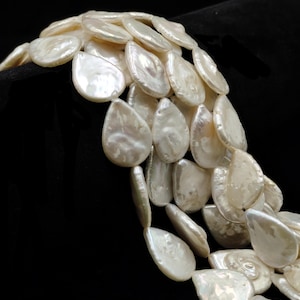 May include: A layered necklace composed of numerous, irregularly shaped, luminous white pearls. The pearls have a smooth, iridescent surface and are strung together to create a cascading effect. The background is solid black, highlighting the necklace's pearly sheen.