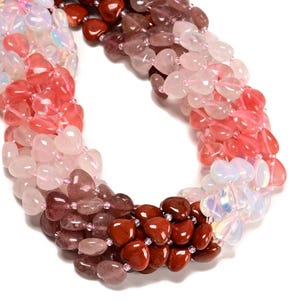 May include: A multi-strand necklace featuring heart-shaped beads in a gradient of colors. The beads transition from a deep reddish-brown to pink, light pink, and iridescent white. The necklace is strung on a delicate, clear cord.
