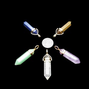 May include: An assortment of gemstone pendants in various colors, including blue, green, yellow, clear, and purple. Each pendant has a gold-colored metal cap and loop. A dime is in the center of the pendants.