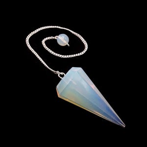 May include: A faceted, opalescent crystal pendulum with a silver chain and a small, round bead. The pendulum is cone-shaped and hangs against a black background. The crystal has a soft, ethereal glow.