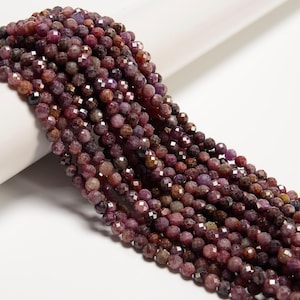 May include: Strands of faceted, round beads in shades of deep red, purple, and brown. The beads have a sparkling, reflective quality, suggesting they are gemstones. The beads are arranged in a flowing, cascading pattern, ideal for jewelry making.